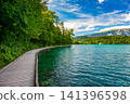 Wooden boardwalk along the shore of Lake Bled in Slovenia, offering a scenic walking route with views of the lake, surrounding forests, and the Julian Alps. 141396598