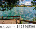 Wooden boardwalk along the shore of Lake Bled in Slovenia, offering a scenic walking route with views of the lake, surrounding forests, and the Julian Alps. 141396599