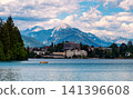Small rowing boat with two unrecognizable people sailing across Lake Bled in Slovenia, with the town of Bled and the majestic Julian Alps rising in the background. 141396608