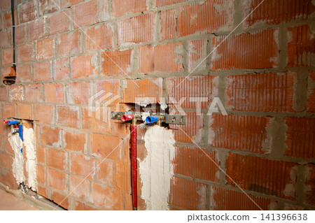 Plumber installing water supply pipes inside unfinished brick wall background Plumber installing water supply pipes inside unfinished brick wall background 141396638