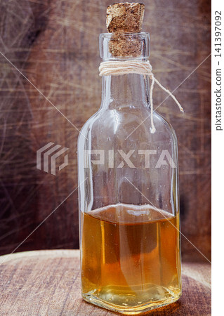 Organic apple cider vinegar in glass bottle with cork and twine, representing healthy cooking, natural seasoning, homemade gourmet food, and wholesome rustic condiment on wooden background Organic apple cider vinegar in glass bottle with cork and twine, representing healthy cooking, natural seasoning, homemade gourmet food, and wholesome rustic condiment on wooden background 141397092