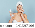 Happy woman in white towel applies skincare product 141397106