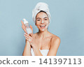 Happy woman showcasing skincare routine against soft blue background 141397113