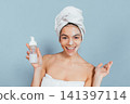 Cheerful woman with face mask, holding bottle against blue background 141397114