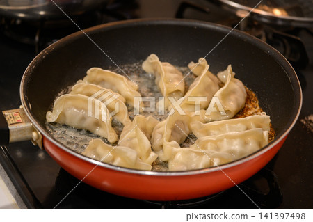 在瓦斯爐上的紅色煎鍋中,將餃子煎至香脆。 在瓦斯爐上的紅色煎鍋中,將餃子煎至香脆。 141397498