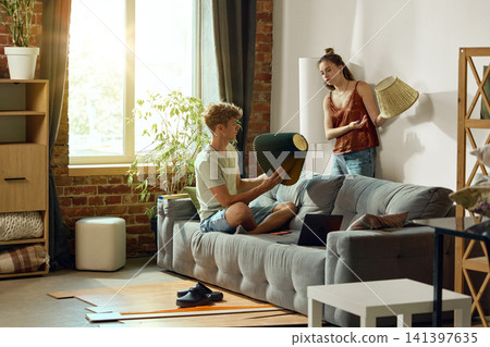 Young couple comparing lampshades while decorating new apartment Young couple comparing lampshades while decorating new apartment 141397635