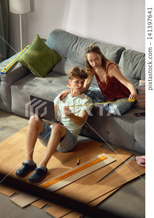 Young couple measuring flooring while browsing products on laptop Young couple measuring flooring while browsing products on laptop 141397641