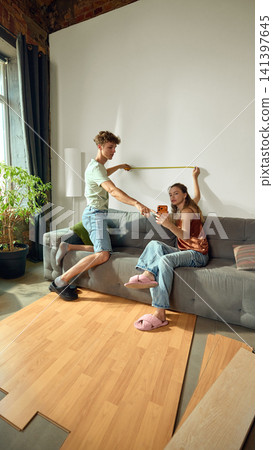 Young couple measuring wall and browsing decor in new apartment Young couple measuring wall and browsing decor in new apartment 141397645