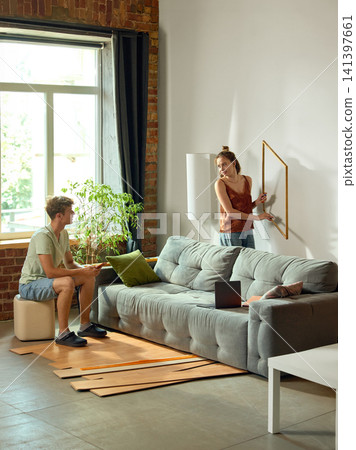Woman positioning wall frame while partner checks measurements Woman positioning wall frame while partner checks measurements 141397661
