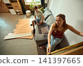 Woman measuring cabinet while partner reviews renovation plans 141397665