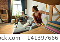 Woman measuring shelf height while partner shops online on laptop 141397666
