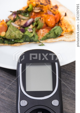 Glucose meter using for checking sugar level and fresh baked vegetarian pizza Glucose meter using for checking sugar level and fresh baked vegetarian pizza 141397991