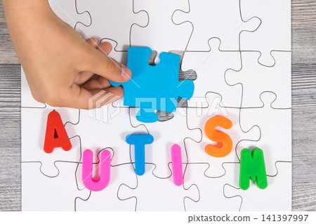 Hand of child putting together white and blue puzzle Hand of child putting together white and blue puzzle 141397997