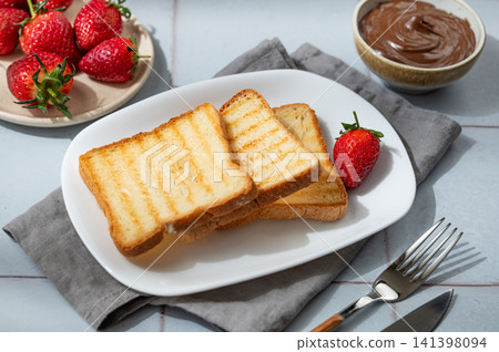 Toasted bread, chocolate cream and strawberry on a plate on a blue tile background 141398094