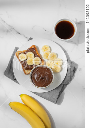 Toasted bread with chocolate cream and banana on a plate on a marble background Toasted bread with chocolate cream and banana on a plate on a marble background 141398102
