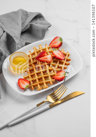 Belgian waffles with fresh strawberries and honey on a white plate on a marble background Belgian waffles with fresh strawberries and honey on a white plate on a marble background 141398107