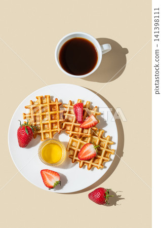 Belgian waffles with fresh strawberries and honey on a white plate on  a yellow background 141398111