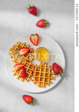 Belgian waffles with fresh strawberries and honey on a white plate on a concrete background 141398112