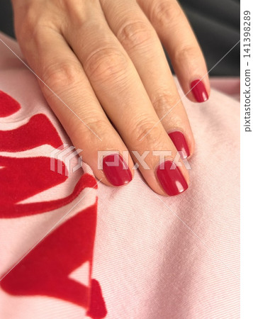 Hand with red nail polish resting on pink and red fabric with soft lighting background 141398289