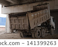 Dirty dump truck with its bed raised under a concrete bridge 141399263