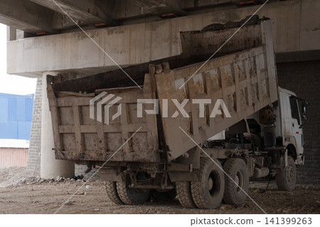 Dirty dump truck with its bed raised under a concrete bridge 141399263