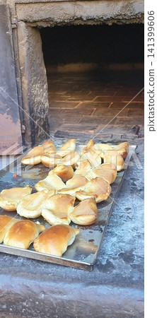 Freshly baked small pies on a baking sheet in front of a traditional stove. Freshly baked small pies on a baking sheet in front of a traditional stove. 141399606