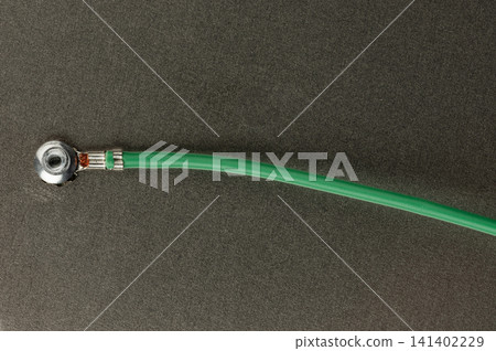 Green cable connected to a metal fitting on a dark surface Green cable connected to a metal fitting on a dark surface 141402229