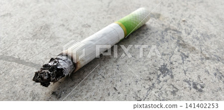 A still-lit cigarette butt with a green filter on a concrete surface. A still-lit cigarette butt with a green filter on a concrete surface. 141402253