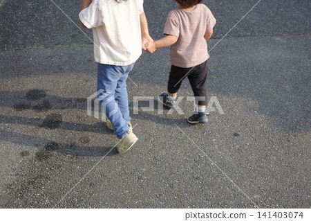 The backs of two children walking down the street, holding hands. The backs of two children walking down the street, holding hands. 141403074