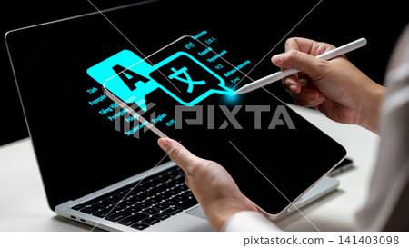 A person uses a stylus on a tablet showing a glowing translation icon interface next to a laptop A person uses a stylus on a tablet showing a glowing translation icon interface next to a laptop 141403098