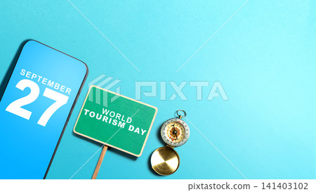 Flat lay of smartphone displaying September 27, a World Tourism Day sign, and a compass on a blue background with copy space 141403102