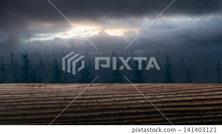 A close-up view of a rustic wooden surface with a soft-focus misty pine forest and dramatic stormy sky in the background, perfect for product display. Horror or Halloween background A close-up view of a rustic wooden surface with a soft-focus misty pine forest and dramatic stormy sky in the background, perfect for product display. Horror or Halloween background 141403121
