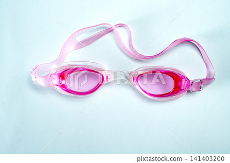 Close-up of bright pink swimming goggles laid on a light blue textured surface. Perfect concept for summer, swimming, and water sports Close-up of bright pink swimming goggles laid on a light blue textured surface. Perfect concept for summer, swimming, and water sports 141403200