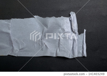 A piece of white, creased paper with jagged, torn edges resting on a dark, textured surface, creating a minimalist high-contrast composition for design use A piece of white, creased paper with jagged, torn edges resting on a dark, textured surface, creating a minimalist high-contrast composition for design use 141403249