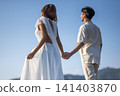 A young Indonesian southeast asian couple in wedding outfits holding hands and walking together against a clear blue sky during an outdoor pre-wedding photo shoot 141403870