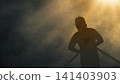 Dramatic silhouette of a man bound in heavy chains, standing under a bright golden light beam illuminating a dark, smoky sky, symbolizing struggle, captivity, and hope of freedom 141403903