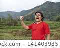 An enthusiastic Indonesian man wearing a red t-shirt and traditional red and white headband cheering with a fist raised in the air. Hari Kemerdekaan Dirgahayu Indonesia 141403935