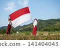 Two Indonesian school children in uniform proudly holding the red and white Indonesian national flag, celebrating national pride. Hari Kemerdekaan, Merdeka, and Dirgahayu Indonesia on 17 Agustus 141404043