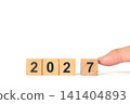 Hand Placing Wooden Number Block 2027 New Year Concept on White Background 141404893