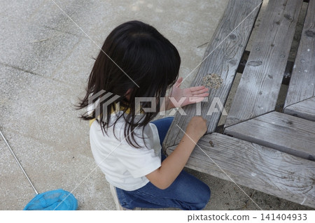 一個孩子坐在公園的木長椅前,玩著鵝卵石。 一個孩子坐在公園的木長椅前,玩著鵝卵石。 141404933