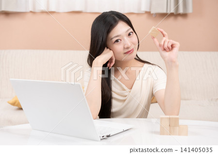 一位年輕女子暢想投資和財富累積:一台筆記型電腦和積木。 一位年輕女子暢想投資和財富累積:一台筆記型電腦和積木。 141405035