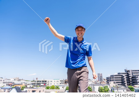 A male truck driver strikes a victory pose against a blue sky. A male truck driver strikes a victory pose against a blue sky. 141405402