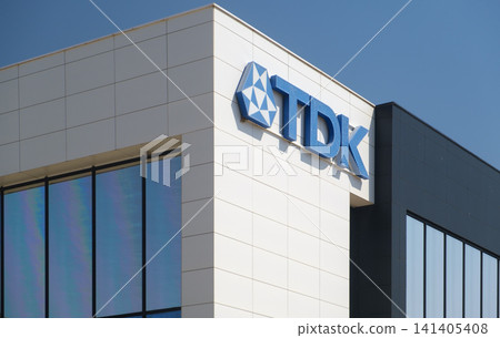 Modern building featuring the TDK logo, sleek architecture with large windows and white panel facade, representing innovation in electronic component manufacturing. Modern building featuring the TDK logo, sleek architecture with large windows and white panel facade, representing innovation in electronic component manufacturing. 141405408