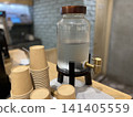 A cold water dispenser and paper cups on the counter. 141405559