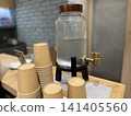 A cold water dispenser and paper cups on the counter. 141405560