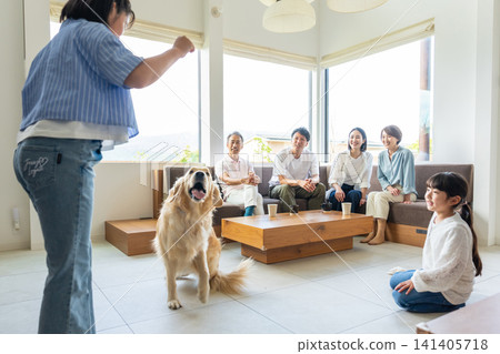 A three-generation family interacting with their dog in the living room. 141405718