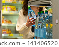 A person selecting a bottle of water from a refrigerated display in a grocery store, showcasing the convenience of hydration and product variety. 141406520