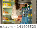 A Person Selecting Bottled Water from a Refrigerated Display Case in a Grocery Store Setting. 141406523
