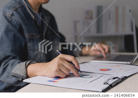 freelancer man hand holding pen pointing at business document paper, analyzing marketing chart and graph data while using laptop. Startup entrepreneur planning financial budget strategy office desk. freelancer man hand holding pen pointing at business document paper, analyzing marketing chart and graph data while using laptop. Startup entrepreneur planning financial budget strategy office desk. 141406654