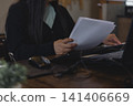 Businesswoman holding and reading business document paper at office desk with computer. Concept of analyzing financial report, reviewing resume, checking legal contract, or doing paperwork. 141406669